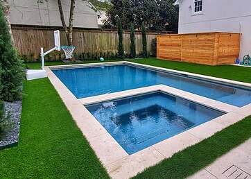 Artificial grass lawn next to large backyard swimming pool 